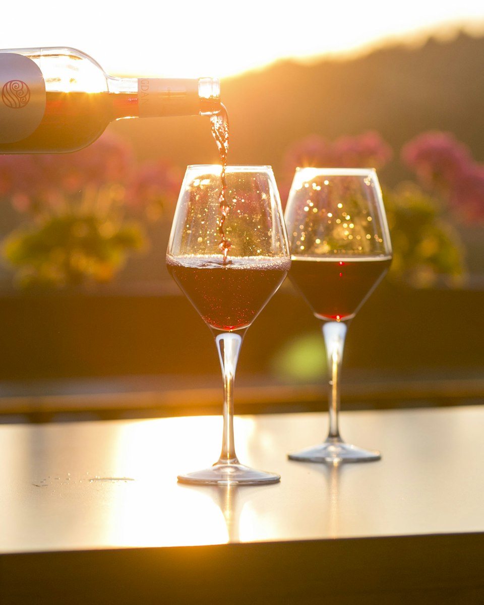 Red wine poured into two glasses at sunset, with flowers behind